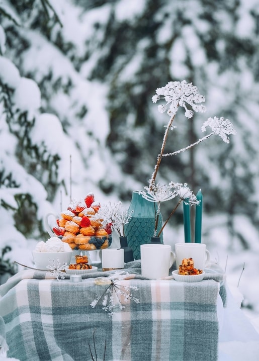 Frosty winter tea table with teal vase, candles, strawberries and pastries in the snow