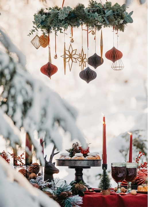 Paper ornaments and stars hanging over a candlelit winter table with pastries and mulled wine