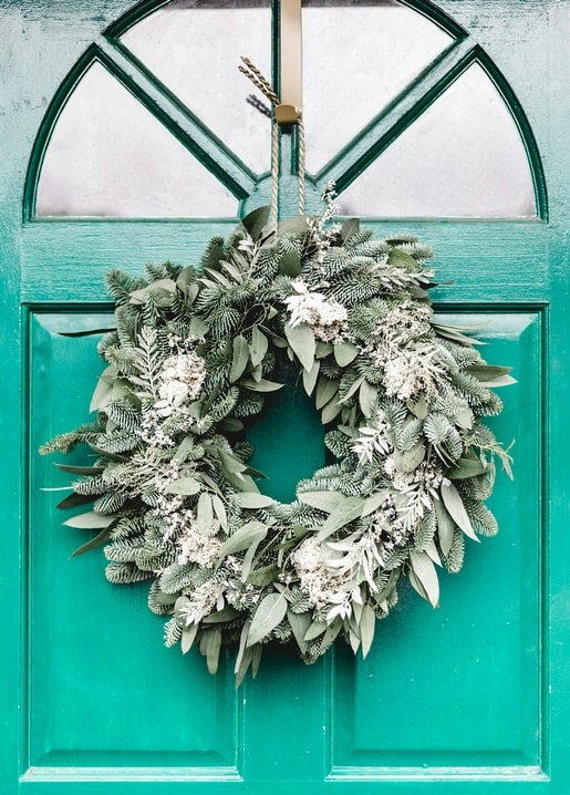 Eucalyptus and pine wreath with dried white blooms hanging on an arched teal door