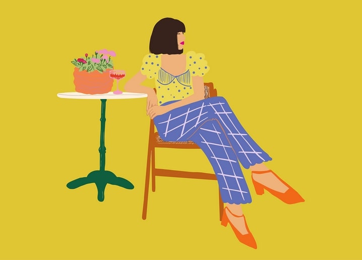 Flat illustration of a woman in plaid trousers seated at a café table on yellow background
