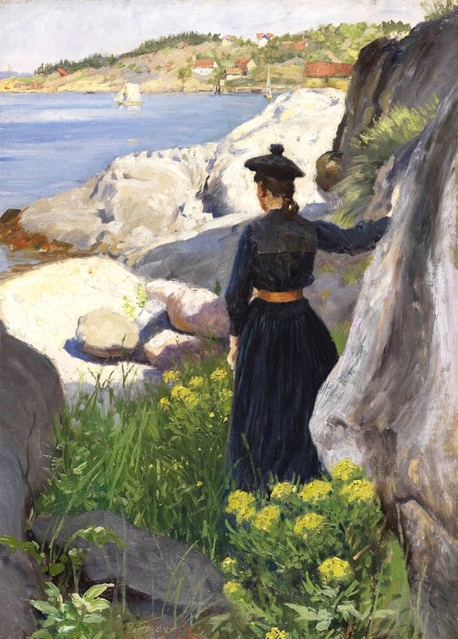 Woman in a dark dress seen from behind standing among coastal rocks, looking out at a sailboat