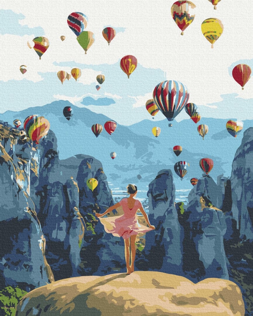 Frau im rosa Kleid beobachtet Heißluftballons über zerklüfteten Felsen
