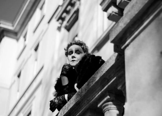 Woman in theatrical stage makeup and lace gloves leaning on a stone balcony rail
