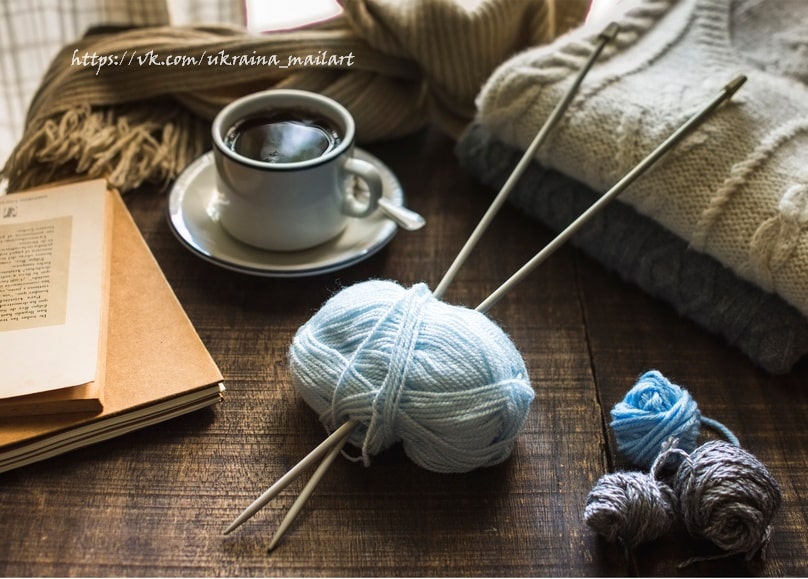 Hellblaues Wollknäuel mit Stricknadeln neben einer Tasse Tee und aufgeschlagenen Büchern