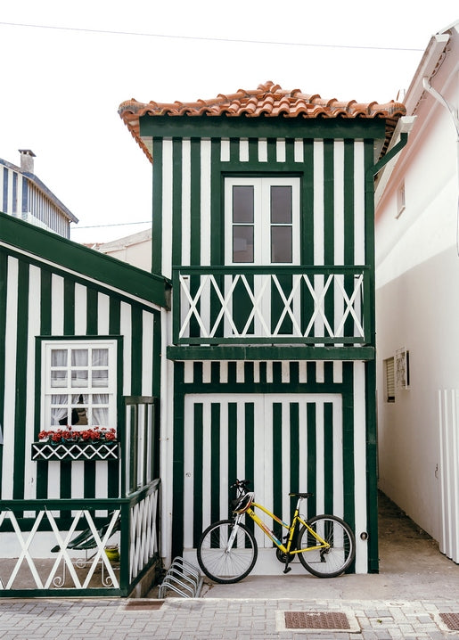 Yellow bicycle parked by a green-and-white striped house with a tiled roof