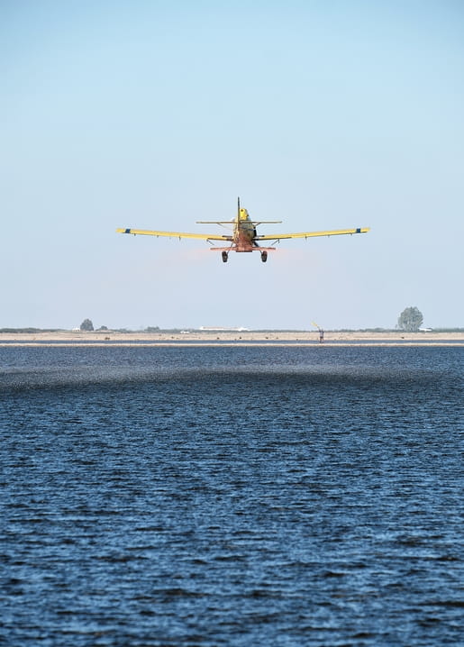 Yellow crop-duster plane banking low over open water at dusk