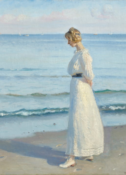 Young woman in a white dress walking along Skagen beach with sailboats on the horizon
