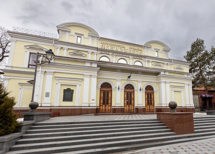 Yellow neoclassical façade of the Zhytomyr Philharmonic building under a cloudy sky