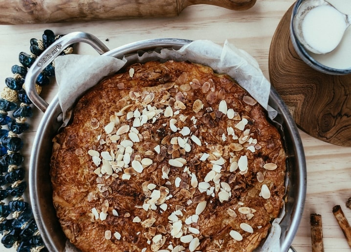 Runder Kuchen mit Mandelblättchen, Nudelholz und Milchkrug auf Holztisch