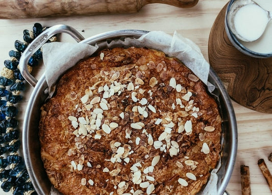 Runder Kuchen mit Mandelblättchen, Nudelholz und Milchkrug auf Holztisch