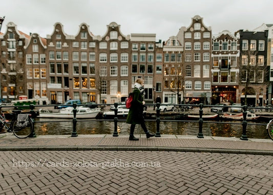 Frau im grünen Mantel spaziert an einer Amsterdamer Gracht mit Giebelhäusern