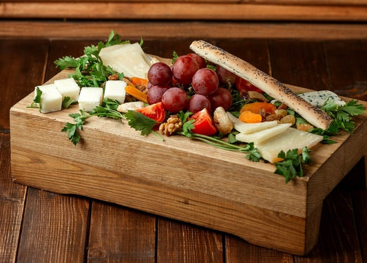 Дошка антипасті з сирними кубиками, виноградом, курагою, горіхами та хлібною паличкою з маком
