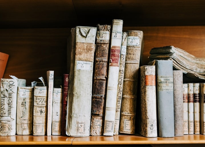 Пошарпані шкіряні та тканинні корінці книг із вицвілими рукописними наліпками на дерев'яній полиці
