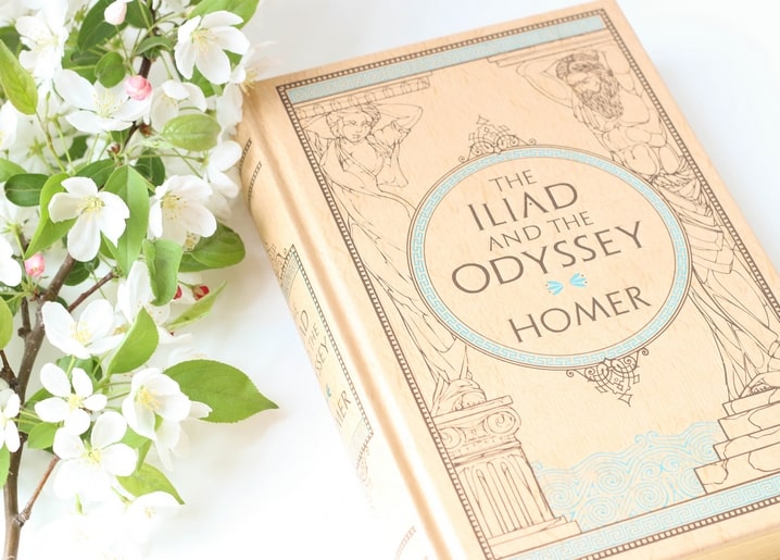 Apple blossom branch beside a hardcover edition of Homer's Iliad and Odyssey