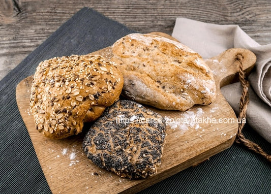 Drei Brötchen auf einem Holzbrett: eines mit Hafer, eines mit Mehl, eines dunkel mit Mohn.