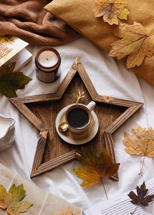Coffee cup in a wooden star-shaped tray with autumn leaves and a candle