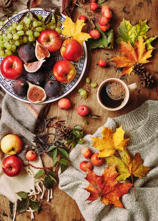 Bowl of apples, figs, and grapes with maple leaves, coffee, and a knitted sweater