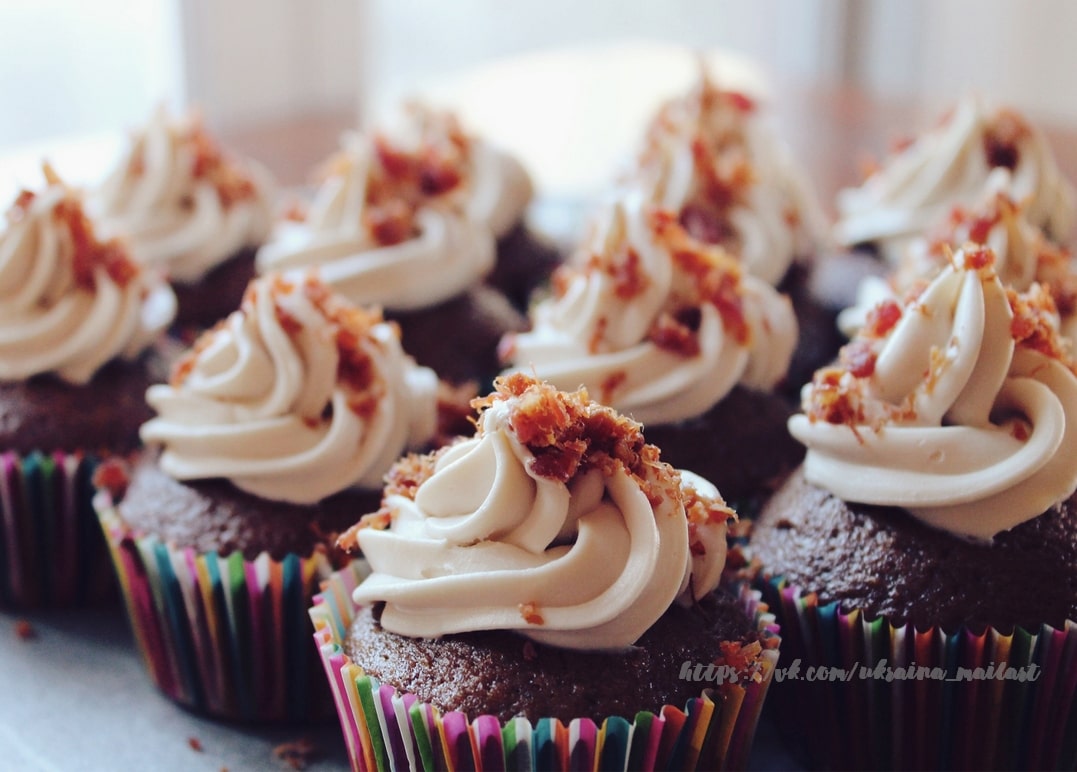 Schokocupcakes mit Sahnehaube und Bacon-Stückchen in bunten Papierförmchen