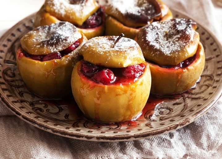 Gebackene Äpfel mit Preiselbeerfüllung und Puderzucker auf einem gemusterten Teller