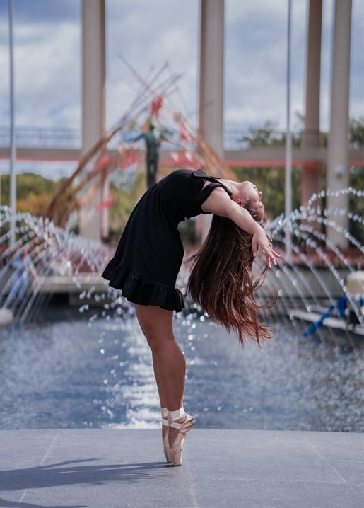 Ballerina auf Spitze beugt sich zurück vor einer Reihe Springbrunnen