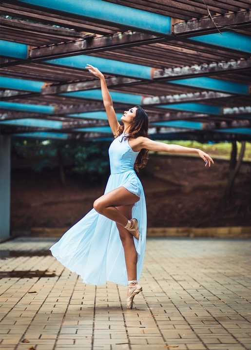 Ballerina in hellblauem Kleid in einer Attitude-Pose unter einer Pergola mit türkisen Balken
