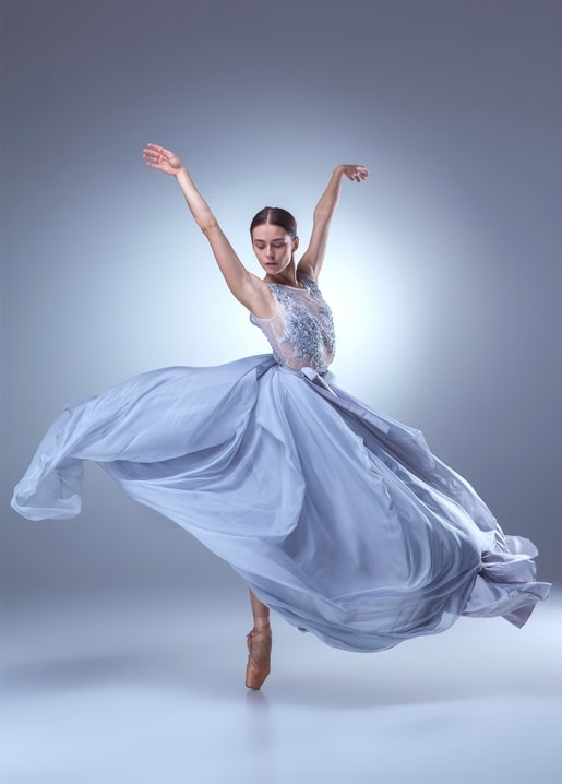 Ballerina wirbelt in einem fließenden graublauen Kleid mit erhobenen Armen
