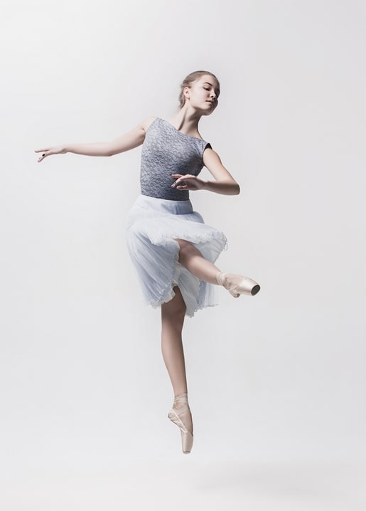 Ballerina im grauen Tüllrock beim Sprung auf Spitzenschuhen vor weißem Studiohintergrund