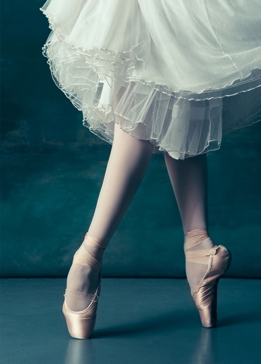 Nahaufnahme gekreuzter Ballerina-Füße in rosa Spitzenschuhen unter weißem Tüll-Tutu
