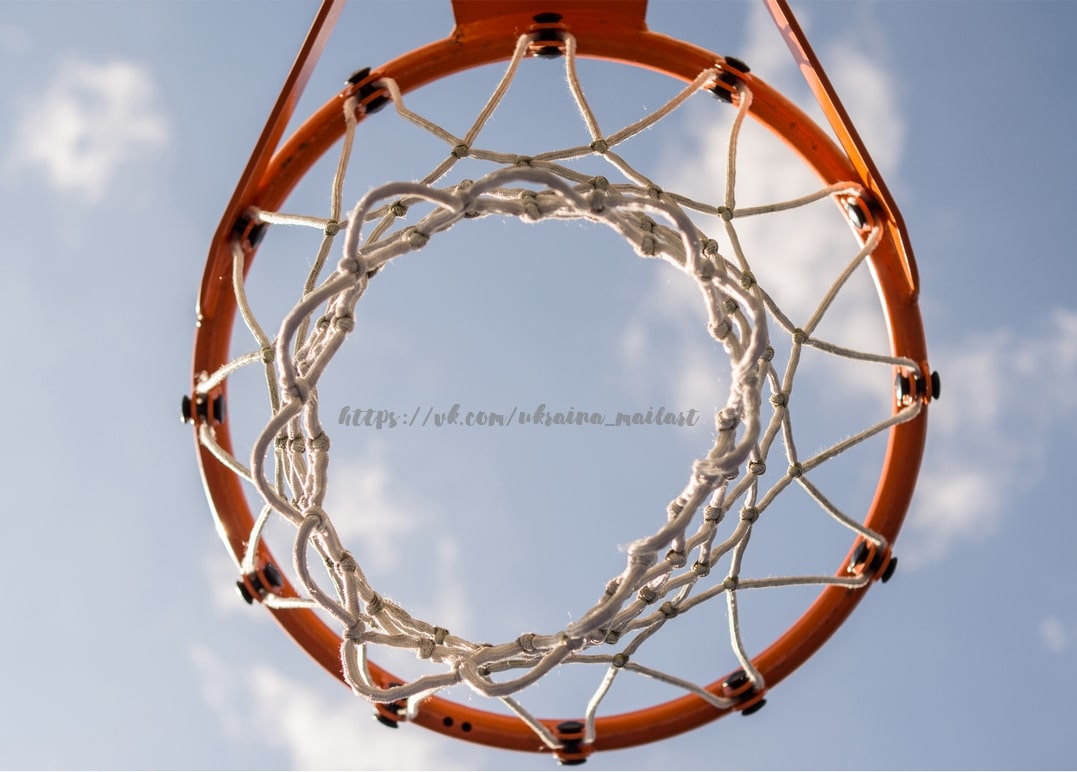 Basketballkorb mit Netz von unten vor blauem Himmel mit Wolken fotografiert