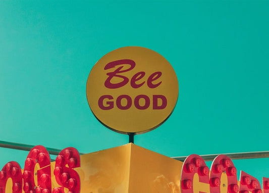 Gelbes „Bee Good“-Schild über einem Jahrmarktstand vor türkisfarbenem Himmel