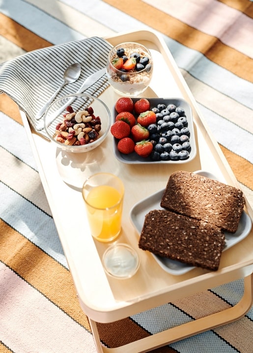Frühstückstablett mit Müsli, Beeren, Nüssen, Orangensaft und Toast auf gestreifter Decke