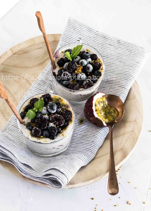 Дві склянки ягідного парфе з ожиною, чорницею, м'ятою та маракуєю, подані з дерев'яними ложками.