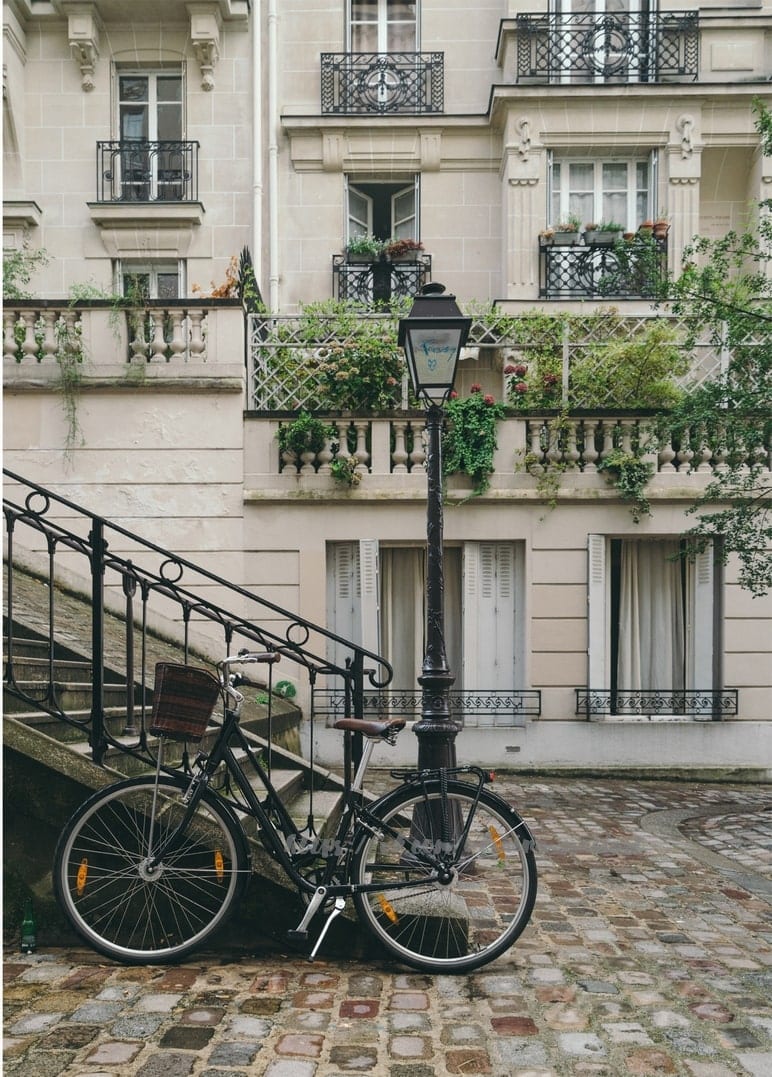 Fahrrad mit Weidenkorb steht an einer Laterne unter efeuumrankten Balkonen einer Pariser Straße