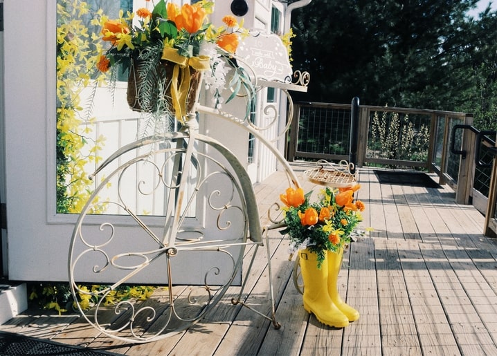 Zierfahrrad und gelbe Gummistiefel als Pflanzgefäß für orangefarbene Tulpen auf einer Terrasse