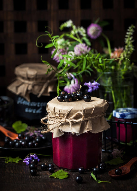 Glas schwarze Johannisbeermarmelade mit Kleeblüten und Beeren, in Papier verschnürt