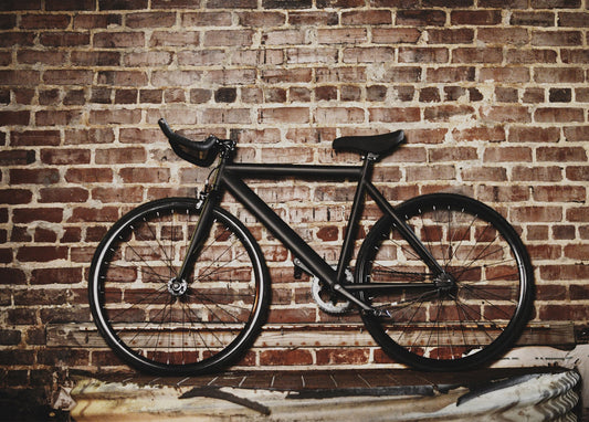 Mattschwarzes Fixie-Rad lehnt an einer verwitterten Backsteinmauer