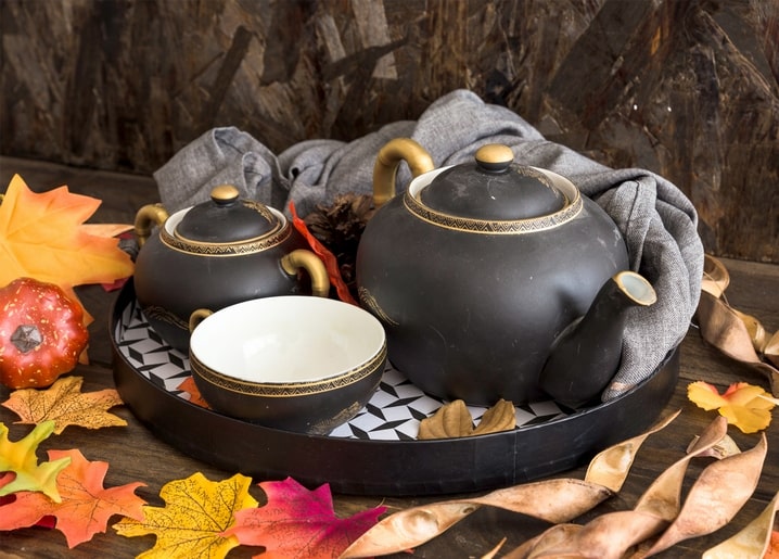 Black-and-gold teapot, sugar bowl and cup on a patterned tray with autumn leaves