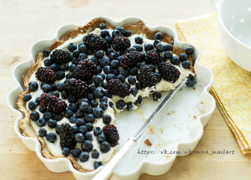 Brombeer-Heidelbeer-Tarte in weißer Förmchen-Form mit einem angeschnittenen Stück auf dem Messer