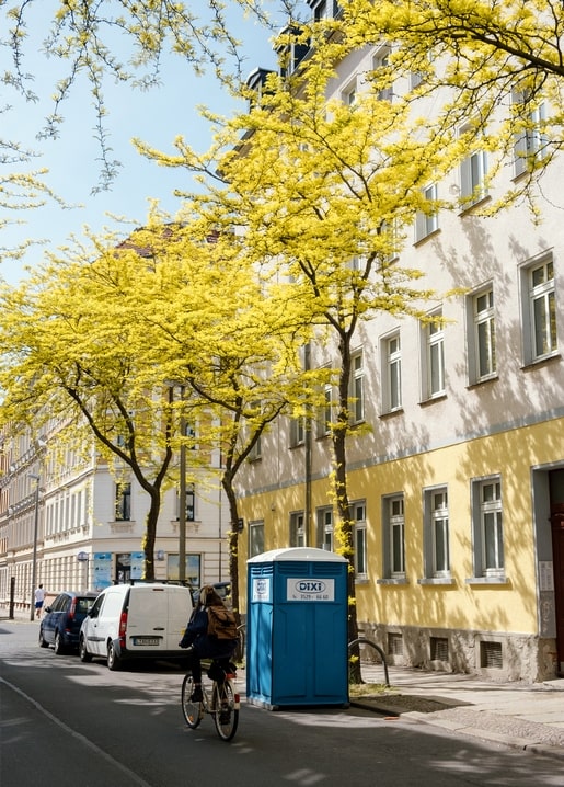 Велосипедистка їде повз квітучі жовті дерева на пастельній міській вулиці