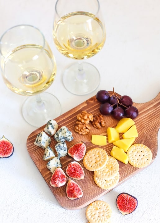 Overhead view of blue cheese, figs, crackers, grapes and two glasses of white wine