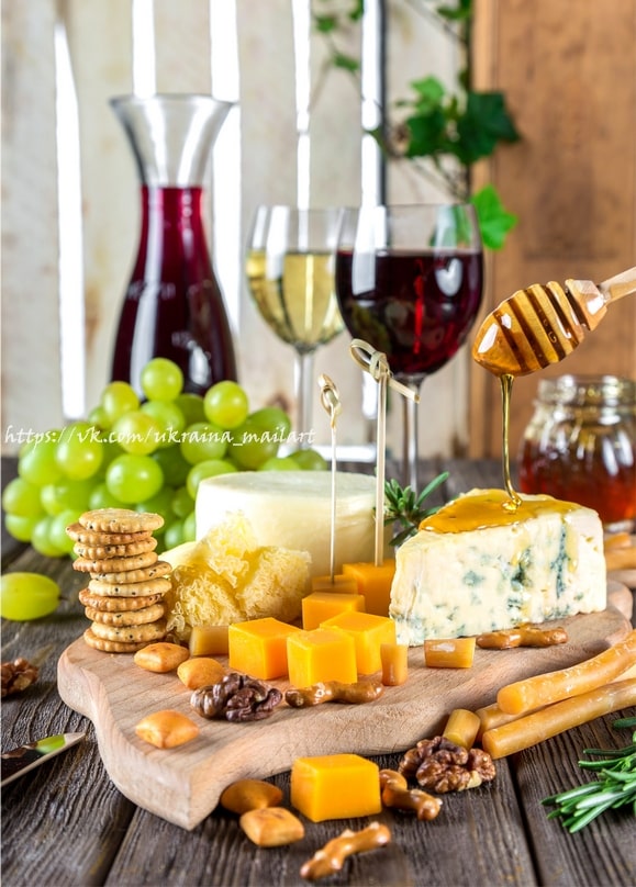 Honey drizzling onto blue cheese with cheddar cubes, walnuts, crackers and two glasses of wine