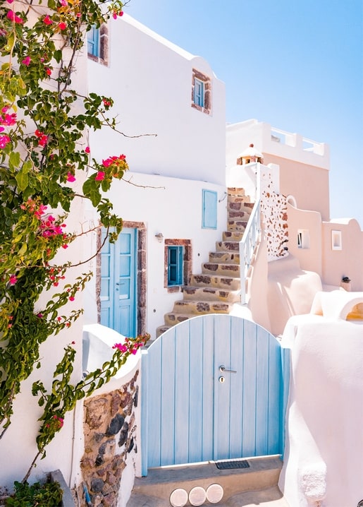 Blaue Tür und Gartentor an einem weißen Haus auf Santorin mit pinker Bougainvillea