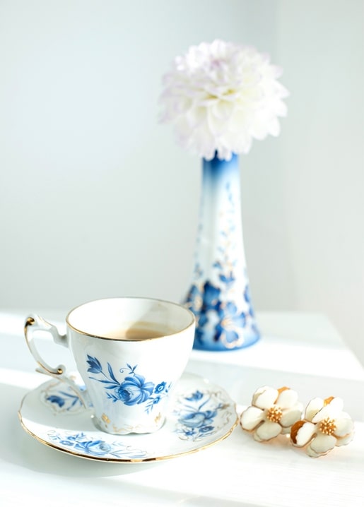 Blau-weiße Teetasse mit Tee neben einer Vase mit weißer Dahlie