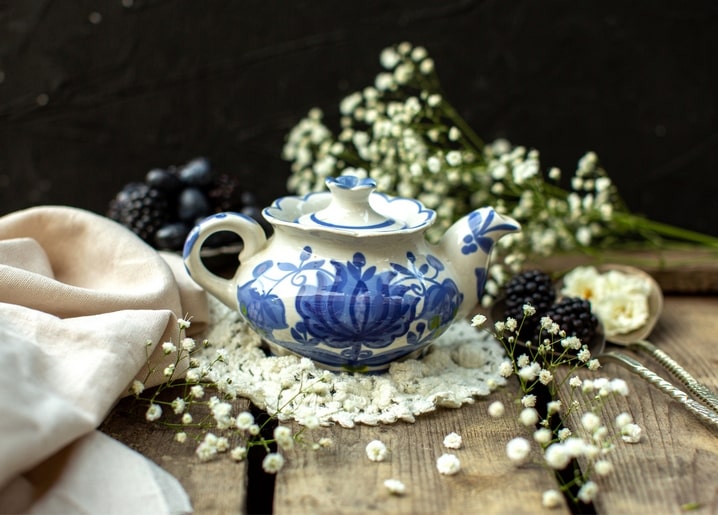 Blue-and-white porcelain teapot beside blackberries and baby's breath flowers