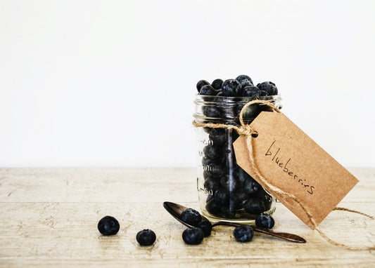 Einweckglas mit Heidelbeeren, Kraftpapier-Etikett und altem Löffel auf Holztisch