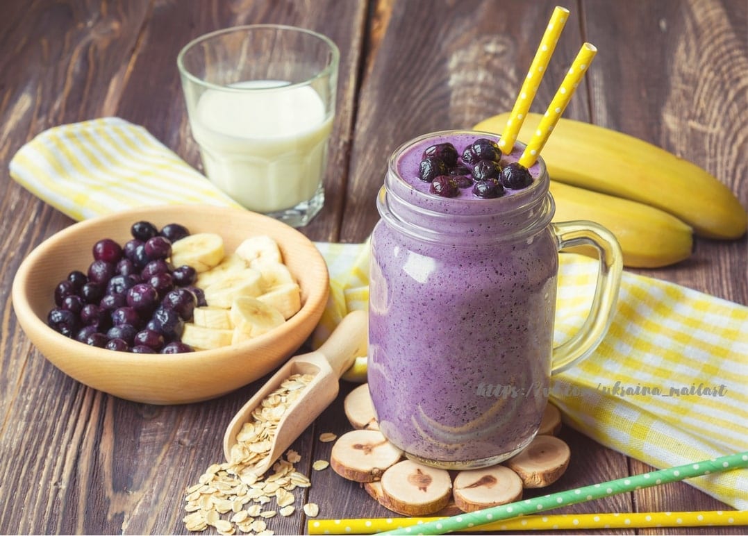 Blaubeer-Bananen-Smoothie im Einmachglas mit gestreiften Strohhalmen, Beeren und Haferflocken