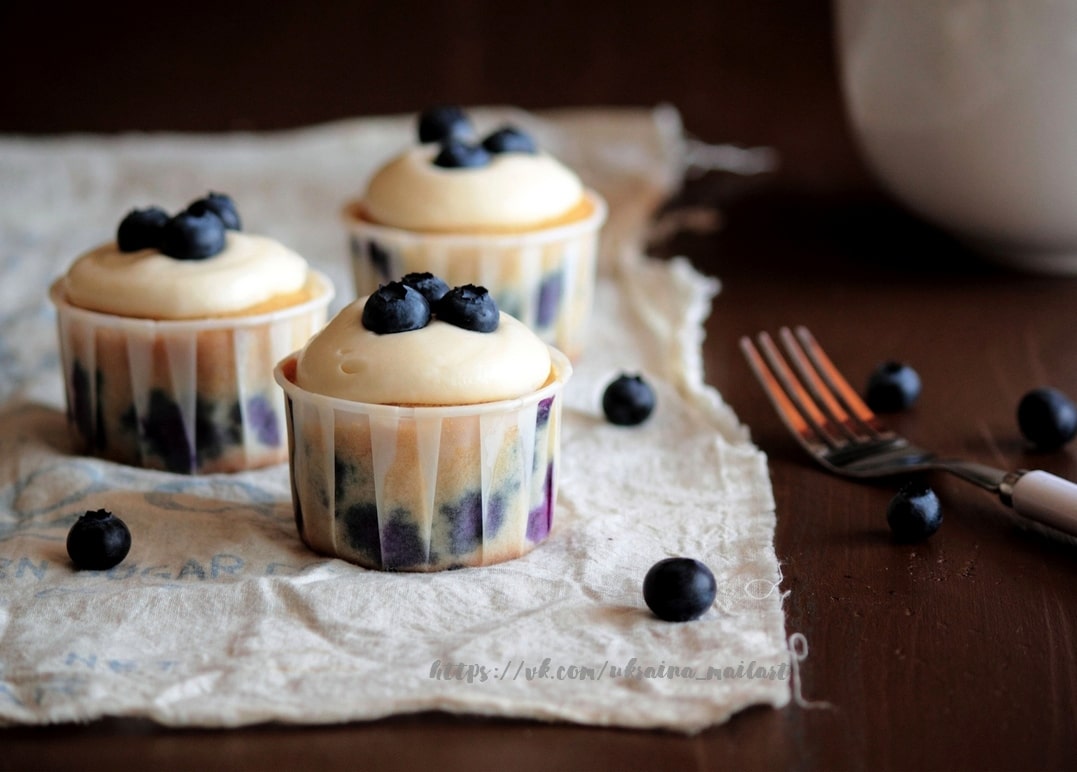 Drei Blaubeer-Cupcakes mit Sahnecreme auf einem Leinentuch mit frischen Beeren