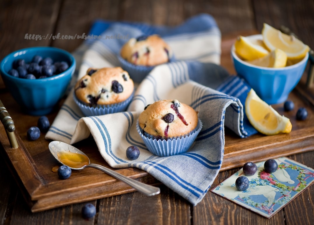 Blaubeermuffins mit Zitronenspalten und einem Löffel Honig auf gestreifter Serviette