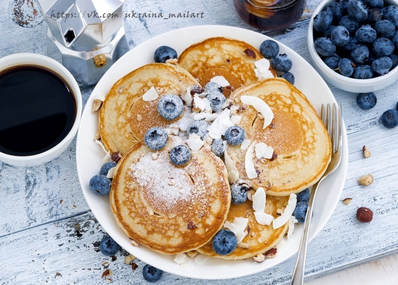 Stack of blueberry pancakes with coconut and hazelnuts beside coffee and a moka pot