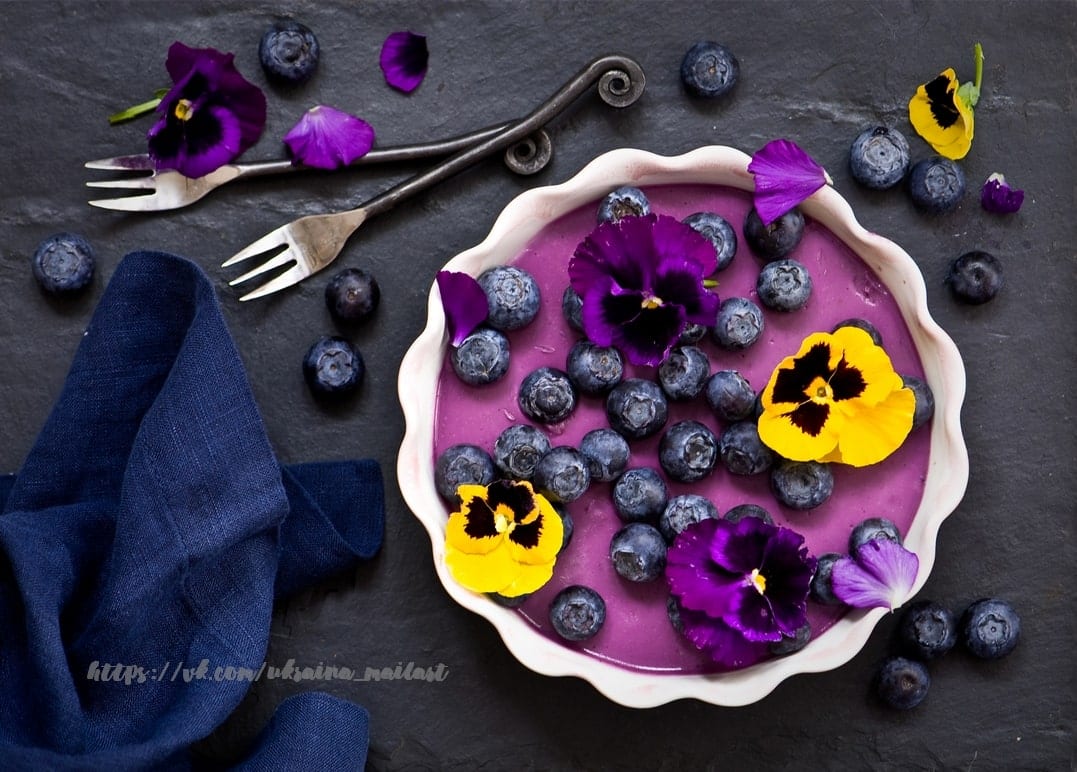Blaubeertarte mit frischen Blaubeeren und Stiefmütterchen auf dunklem Schiefer